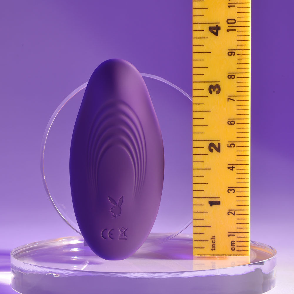 Back view of the purple Playboy Pleasure 'Our Little Secret' vibrating panties displayed with a ruler for size reference, set against a purple background | Flirty Bay adult store and lingerie store