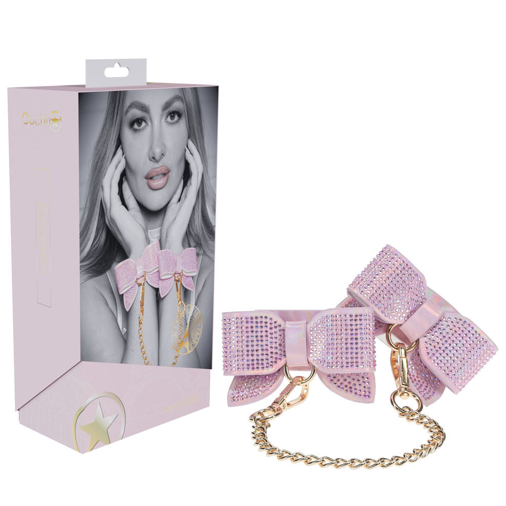 Pink rhinestone bow handcuffs from the Ouch! Paris Collection, featuring holographic bonded leather and gold chain, displayed with packaging | Flirty Bay online adult store, adult toys and lingerie