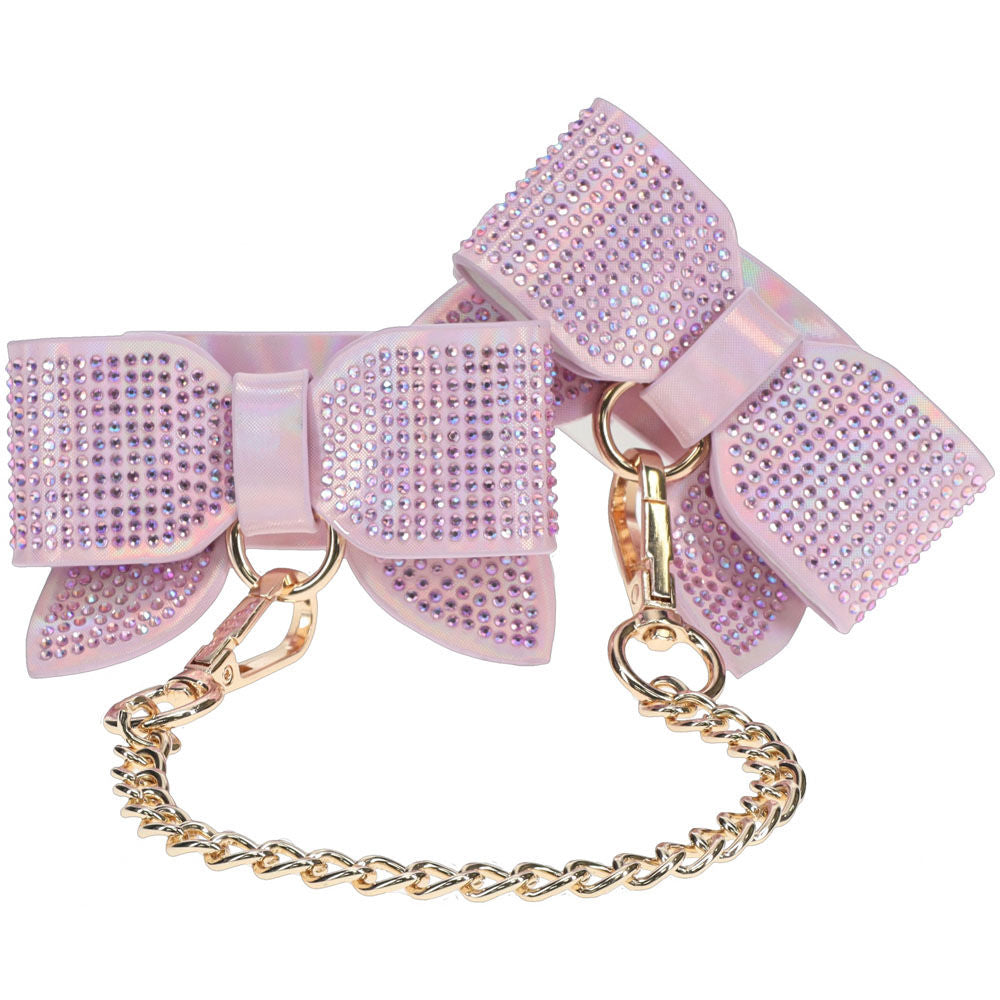 Pink rhinestone bow handcuffs from the Ouch! Paris Collection, featuring holographic bonded leather and gold chain, focus view | Flirty Bay online adult store, adult toys and lingerie