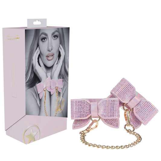 Pink rhinestone bow sex handcuffs from the Ouch! Paris Collection, featuring holographic bonded leather and gold chain, displayed with packaging | Flirty Bay online adult store, adult toys and lingerie