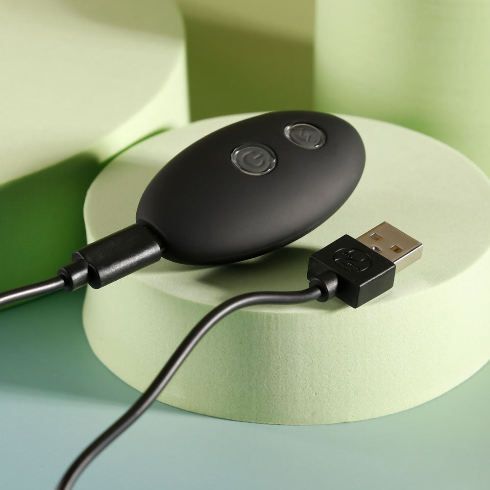 Top view of wireless remote control for vibrating anal beads with charger displayed on decorative yellow-greyish background | Flirty Bay, anal plug adult store Australia