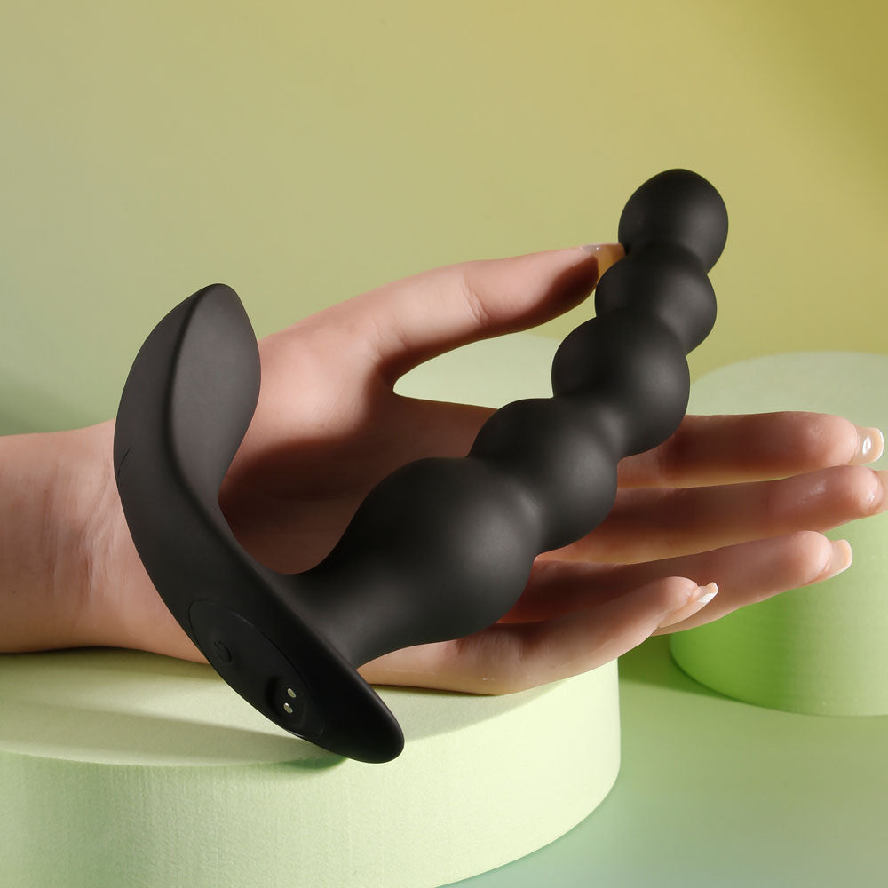 Black Vibrating anal beads held in hand to show flexibility and size for comfortable use, on decorative yellow-greyish background | Flirty Bay, anal plug adult store Australia