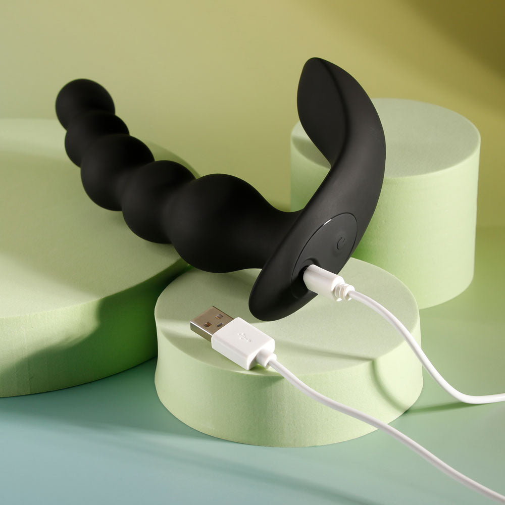 Top view of vibrating anal beads with USB charger connection on decorative yellow-greyish background | Flirty Bay, anal plug adult store Australia