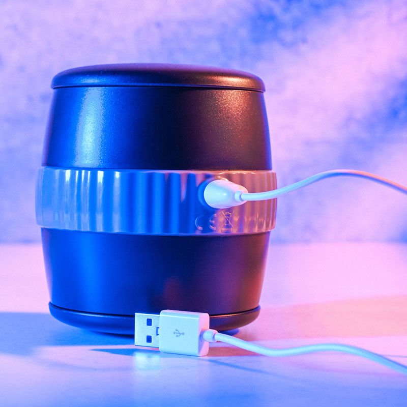 Front view of the Gender X Barrel Of Fun Stroker Male Masturbator highlighting the magnetic charging port, displayed on a blue decorative background. | Flirty Bay adult store Perth